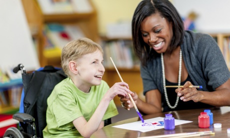 A young woman helps a boy with his painting