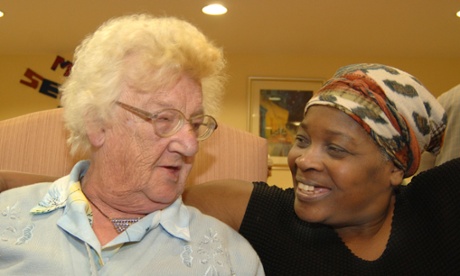 A care assistant chats to an elderly lady in her chair in a multicultural day centre