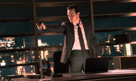 Andrew Scott as Max Denbigh in Spectre points a gun in a high rise office, windows behind him, a hard expression on his face.