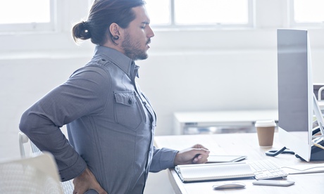 An office worker suffers back pain at his desk.