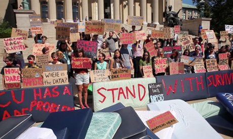 Hunting Ground film still shows students protesting, holding placards and standing in front of  mattresses and a big banner saying Stand With Survivors