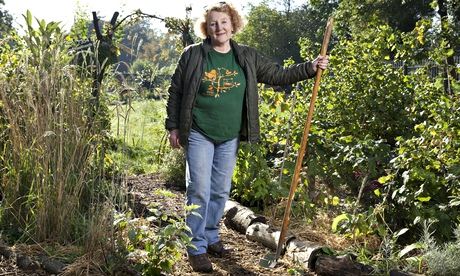Mary slightly smiling, back to the sun, sunglasses pushed back on her head, holding a rake