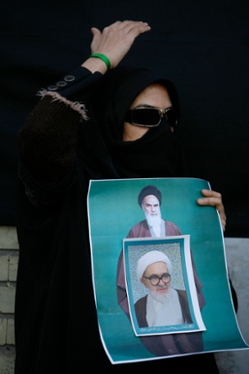 A supporter of the Green Movement mourns the death of Grand Ayatollah Montazeri, the spiritual father of Iran’s reform movement, shown in a poster pasted over a larger one of Ayatollah Khomeini. She covers her face to avoid identification by security, in the city of Qom.