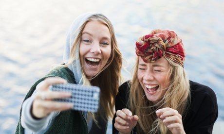 Two young women laughing and filming themselves with a mobile phone.