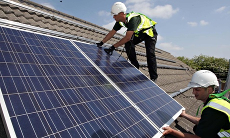 Workmen install solar panels on to the roofs of homes in Delabole
