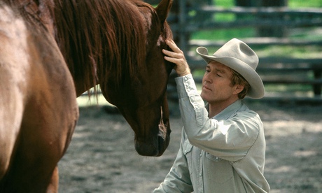 Robert Redford kneeling, his face close to a horse's