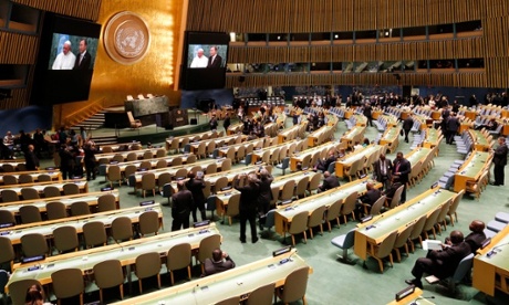 Delegates take photos from the floor and watch television monitors as Pope Francis poses with United Nations Secretary General Ban Ki-Moon.