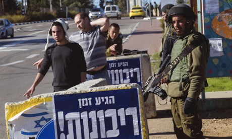 An Israeli soldier guards hitch hikers at the Gush Etzion junction in the occupied West Bank.