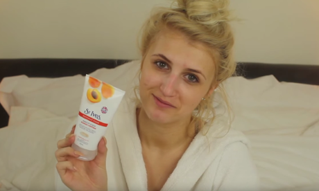 Maddie Burns holds a cosmetics product as she wears a towelling robe sitting on her bed