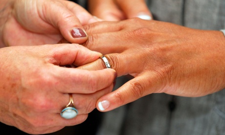 Female couple holding hands & placing ring on finger during their civil partnership ceremony, London.