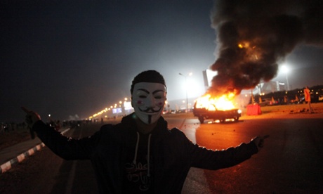 A Zamalek supporter wearing a Guy Fawkes mask near a burning police car outside the stadium in Cairo.