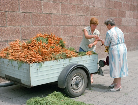 A trader in East Berlin sells her only ware, carrots, from a cart.