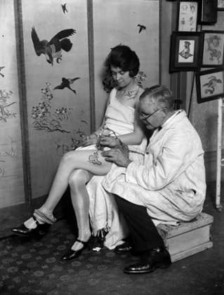 March 1928:  A woman having an image of a snake tattooed onto her thigh by tattooist, George Burchett.