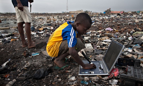 A boy on a rubbish heap looking at an old laptop