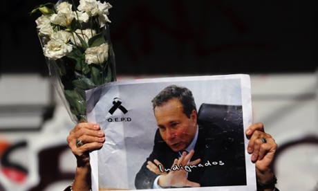 A woman holds up flowers and an picture of late prosecutor Alberto Nisman on the route of his funeral procession.