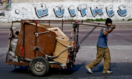 A rubbish recycler in Buenos Aires passes a sign that reads 'vultures' 