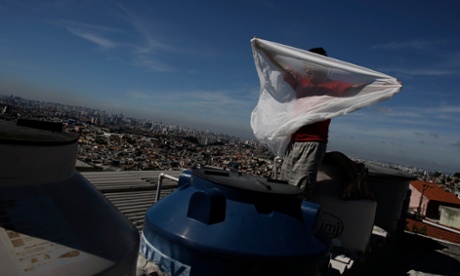 A man places a mosquito net over a water container on his roof. Brazilians are hoarding water in their apartments, drilling homemade wells and taking other emergency measures to prepare for forced water rationing.