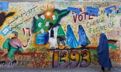 An Afghan woman walks past a wall with graffiti encouraging people to vote in the 2014 presidential elections