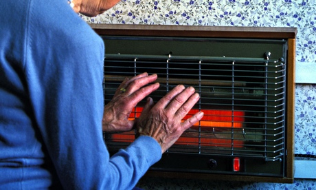 An elderly lady holding her hands near an electric fire.