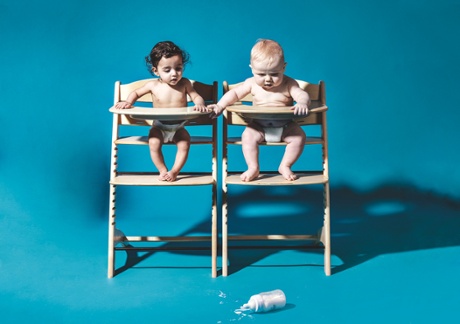 Two model babies in high chairs looking at a dropped bottle of milk on the floor