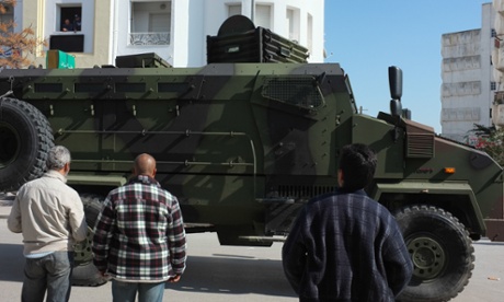 A big green and black tank drives through the streets of Tunis as local people watch