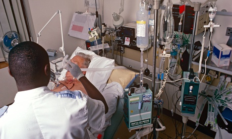 A male staff nurse giving oxygen to a patient in the intensive care unit of a London Hospital, UK