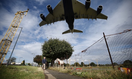 A passenger plane comes into land over a field containing horses near Heathrow.