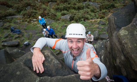 A happy man rock climbing, holding his thumb up in approval