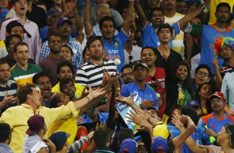 Cricket fans scramble to catch a ball hit for six.