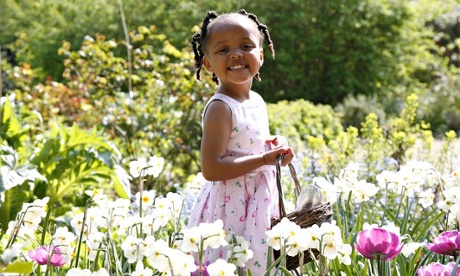 Girl (2-4) collecting flowers and Easter Eggs in garden, smiling