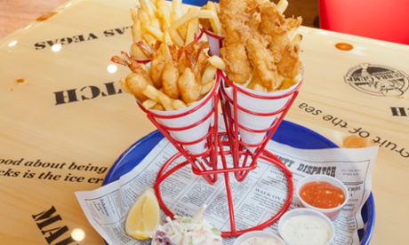Metal holder containing paper cones of breaded shrimp, fried battered fish and 'hush pups' with sauces below in plastic cups
