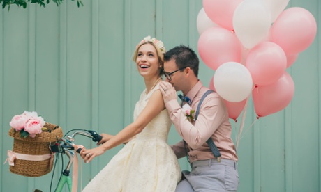 A couple on their wedding day on a bike with pink and white balloons