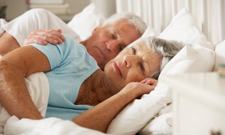 Older woman awake in bed with her husband (posed by models)