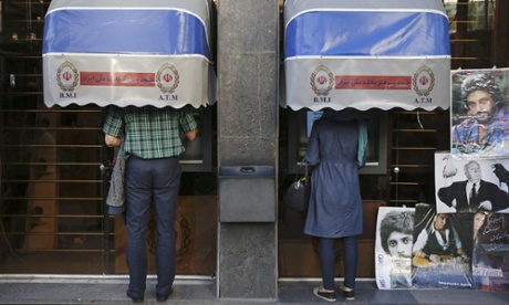 Iranians use ATM machines of Bank Melli Iran in downtown Tehran, Iran. Posters at right, placed by a vendor, show Iranian singers Daryoush, top, Shadmehr Aghili bottom, and British film director Alfred Hitchcock at center.
