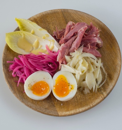 Round wooden bowl with shredded ham hock, a halved boiled egg and endive with vinaigrette.