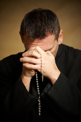 Praying priest with rosary in his hands.