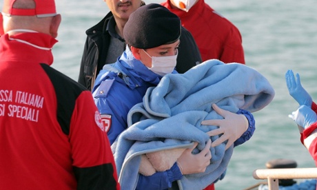 A Red Cross volunteer carries a baby wrapped in a blanket at Porto Empedocle harbour, Sicily.