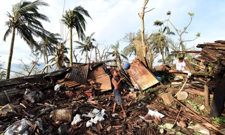 A young boy plays with a ball as his mother searches through the ruins of their family home in Port Vila, Vanuatu.