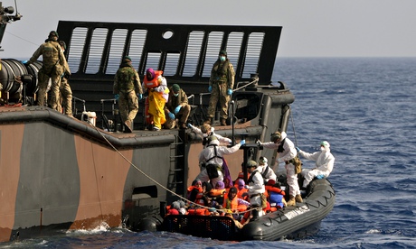 Personnel fhelp refugees adrift in the Mediterranean on to a Royal Navy landing craft