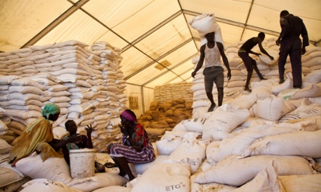 Men carry bags of food while women wait for their rations at the United Nations World Food Programme (WFP) food distribution site in Pibor, South Sudan