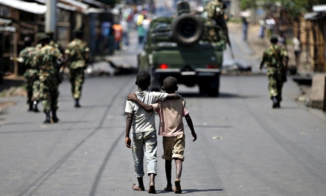 Boys walk behind patrolling soldiers in Bujumbura