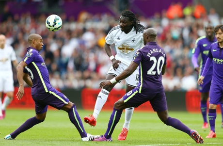 Bafetibis Gomis heads the ball as he's closed down by Fernandinho and Mangala.
