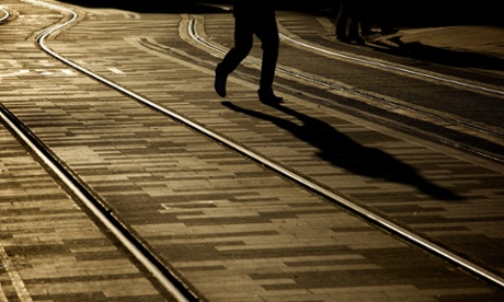 Silhouette of a man walking between tram tracks.