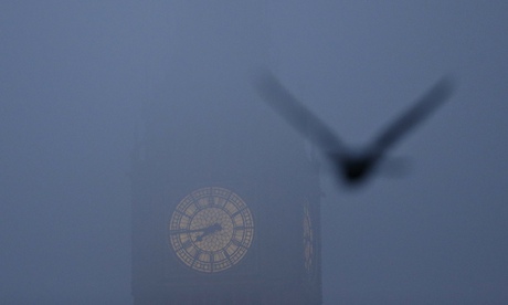 A bird flies past the Big Ben clock tower on a foggy morning in central London