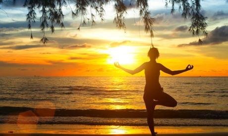 A woman meditates on a beach in Thailand.