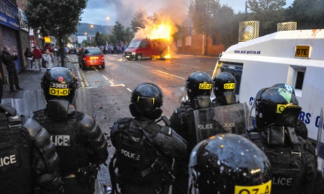 PSNI officers watch as a van burns in the middle of Shankill Road: seven officers forced to leave their homes due to republican threats may soon lose their rent allowances.