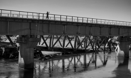 A destroyed bridge in Angola with a shell beneath it and a boy standing on top. 