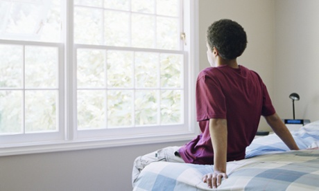 Teenage boy (16-18) sitting on bed, looking out window, rear view