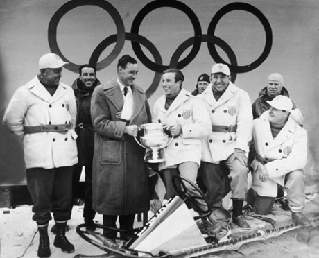 German bobsledder Werner Zahn presents the Olympic trophy to Fiske, while the rest of the four-man winning American bobsled team looks on.