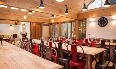 Wooden arched beams and long tables with metal chairs in the dining room in the Flint Barns at Rathfinny Estate in Sussex